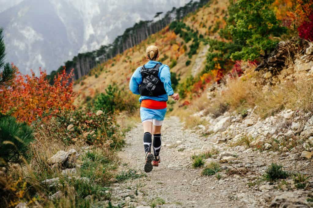 anti-blister socks: view back young female runner runs mountain trail  in autumn forest. compression socks in feet