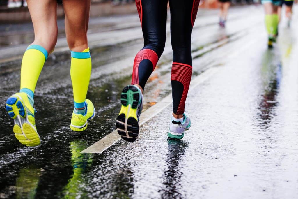 anti-blister socks: feet two girls athletes running on wet street urban marathon