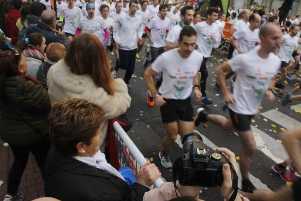 runners dressed in white shirts in a marathon with people cheering on the side and taking photos 