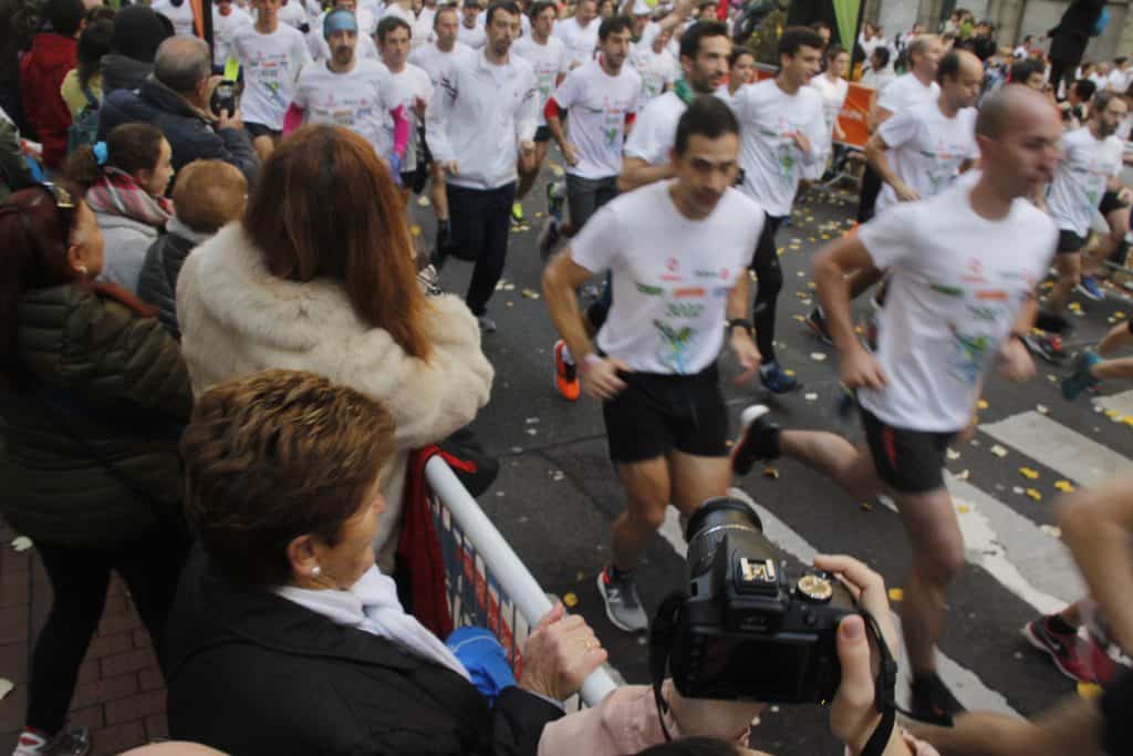 runners dressed in white shirts in a marathon with people cheering on the side and taking photos