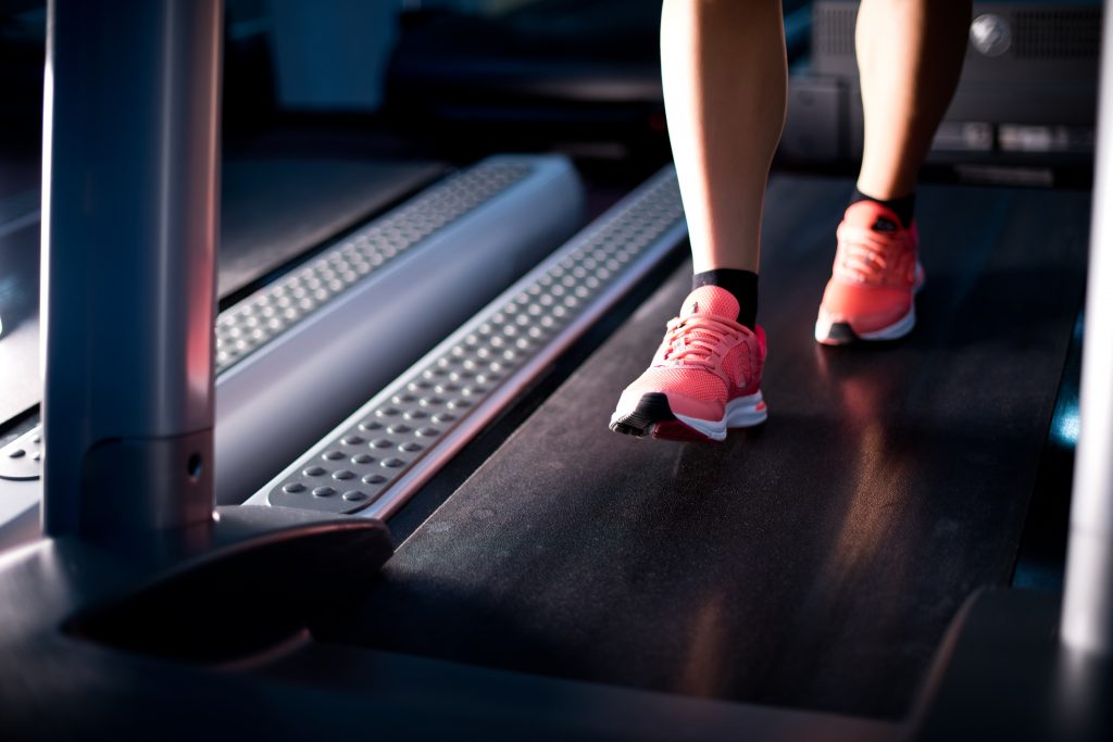 How to Prepare for a 5k in 13 Weeks: legs of a girl who is warming up on a treadmill. Selective focus