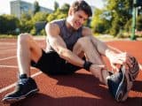 Young male runner suffering from leg cramp on the track at the stadium