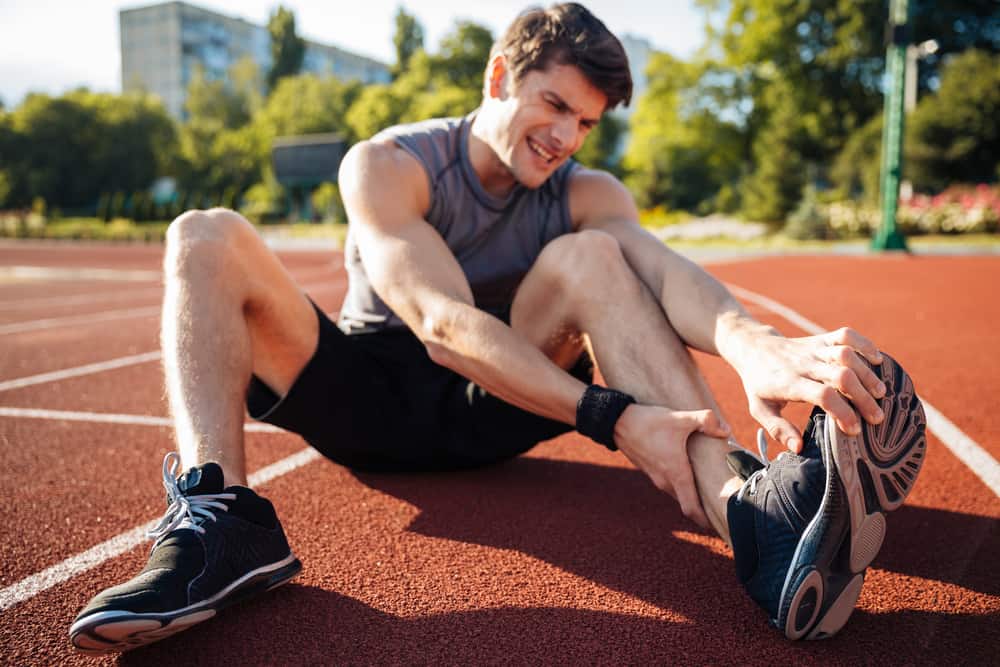 Young male runner suffering from leg cramp on the track at the stadium