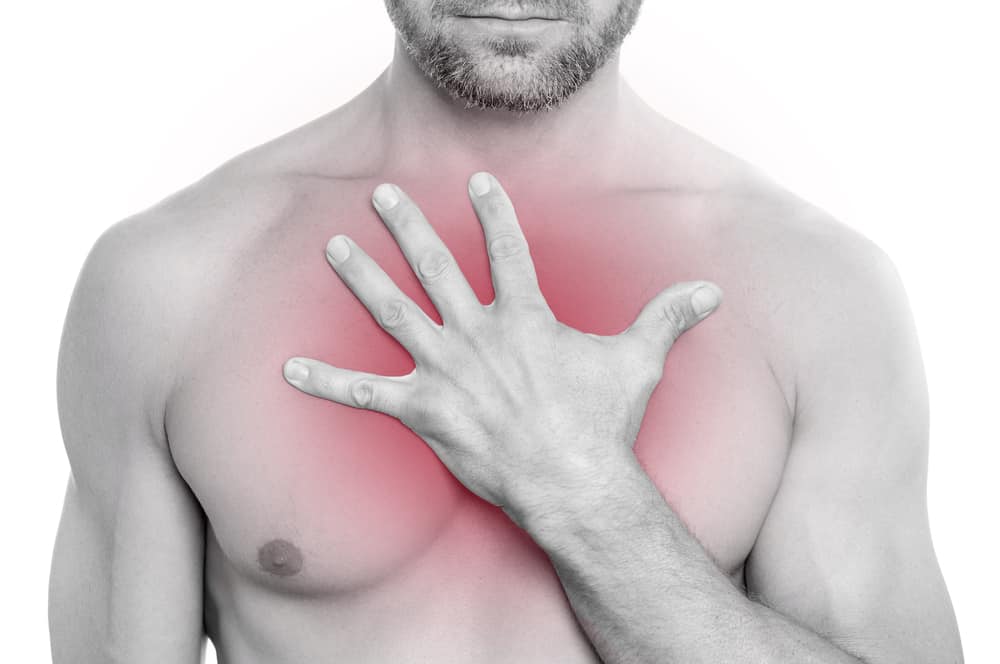 Closeup of shirtless bearded muscular Caucasian man with chest pain; pressing hand on chest on white background