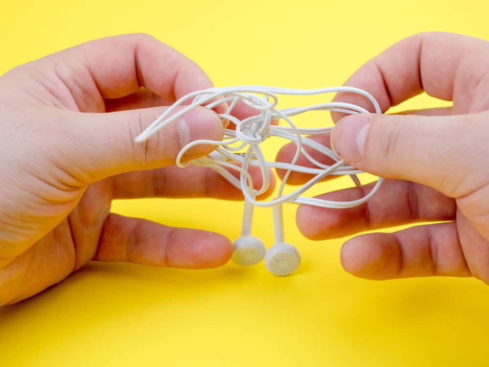 someone untangling headphones with yellow background