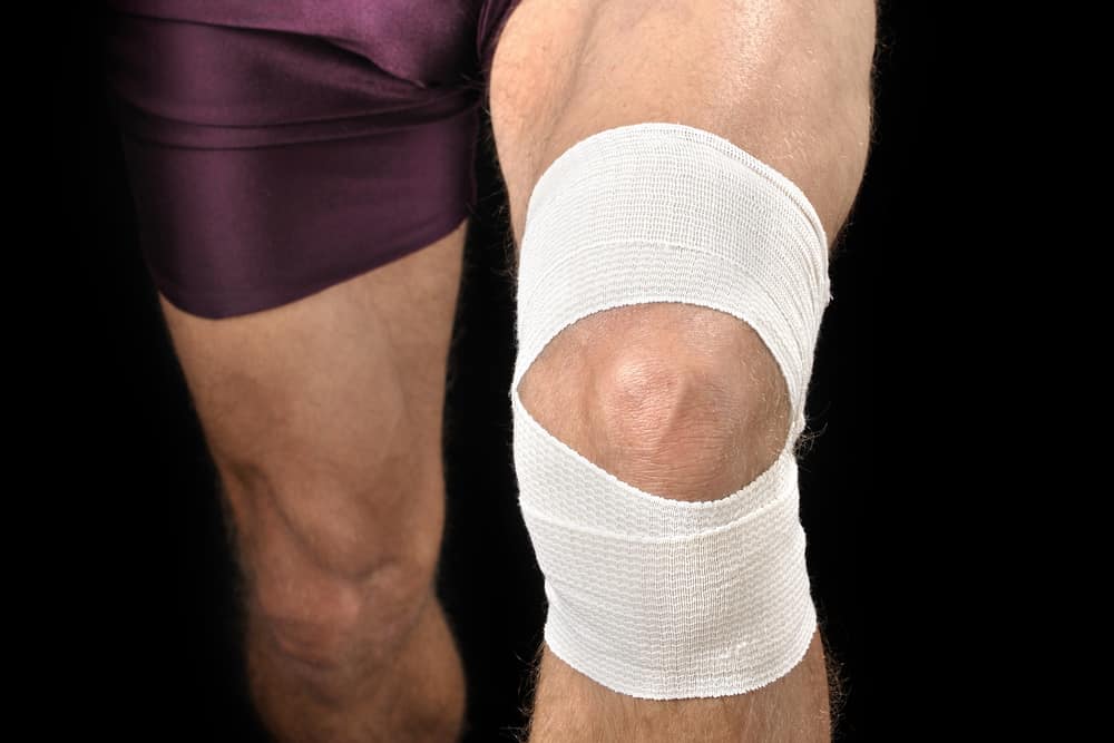 Front closeup of knee of athletic man with white sports wrap on black background