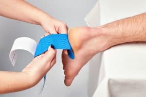 doctor physiotherapist hands applying kinesiology tape on the ankle of a caucasian man. Closeup view