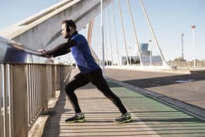 How Many Calories Does Running 2 Miles Burn: man stretching on a bridge railing. sport concept