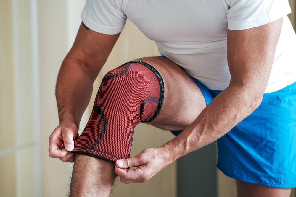 A man puts a sports knee pad on an injured knee before training.