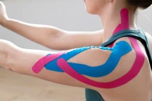Closeup of a young fit womens shoulder with elastic therapeutic kinetic tape on her shoulder. Performing exercise at home. Kinesiology physical therapy.