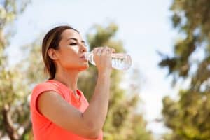Young Hispanic woman drinking water from a bottle and cooling off after her workout