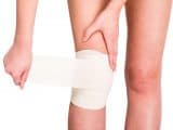 Female is wrapping her knee injury with bandage.