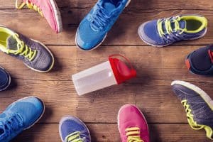 variety of running shoes on a wooden floor with a water bottle in the middle