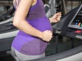 Mid section of pregnant woman running on treadmill at the gym