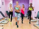 Women wearing cool sports outfits while running on the spot during HIIT workout class with an experienced female fitness instructor indoors