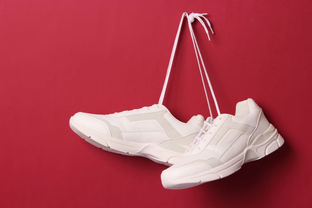 white sneakers hung on a nail from the laces on a red wall