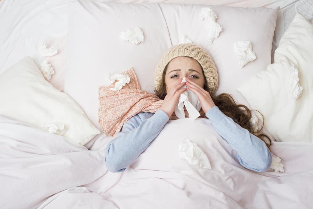 woman in bed blowing her nose, surrounded by tissues