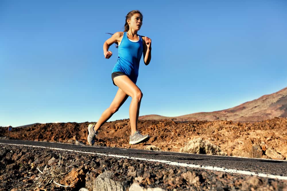 How Many Calories Do 20 Minutes of Running Burn: Running sprinting woman - female runner training outdoors jogging on mountain road in amazing landscape nature. Fit beautiful fitness model working out for marathon outside in summer.