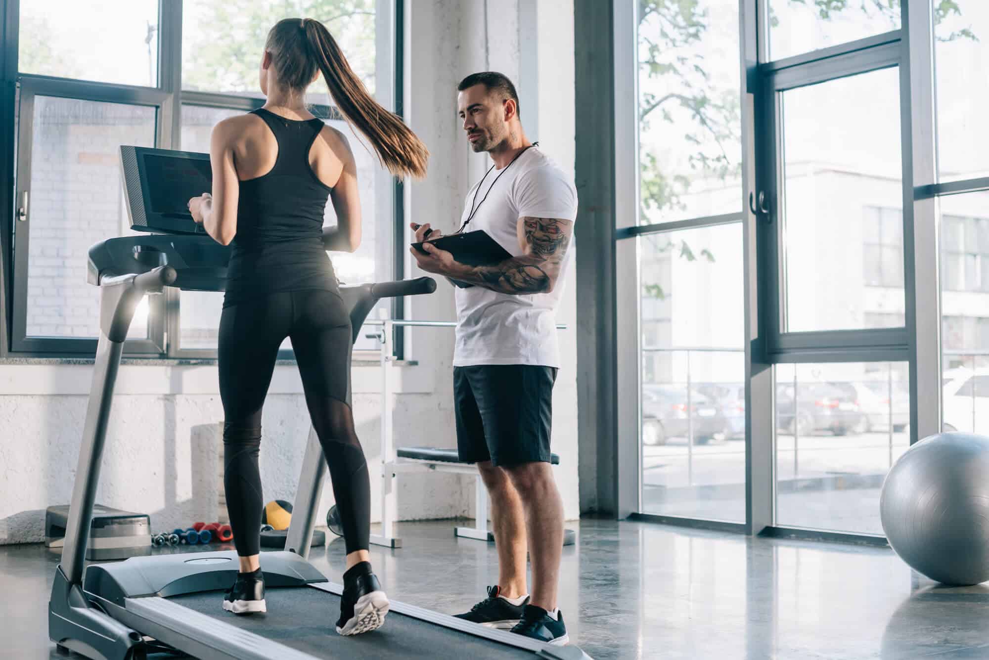 What to Do Before Starting to Train for a Marathon: Personal trainer using timer while sportswoman is running on treadmill