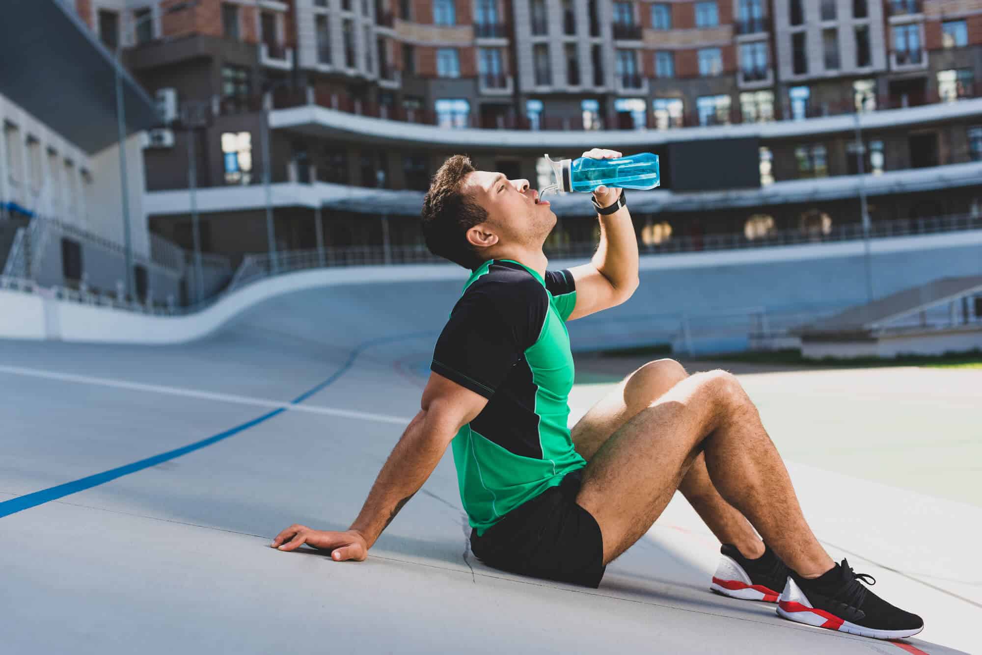 Sportsman drinking water while sitting on the ground 